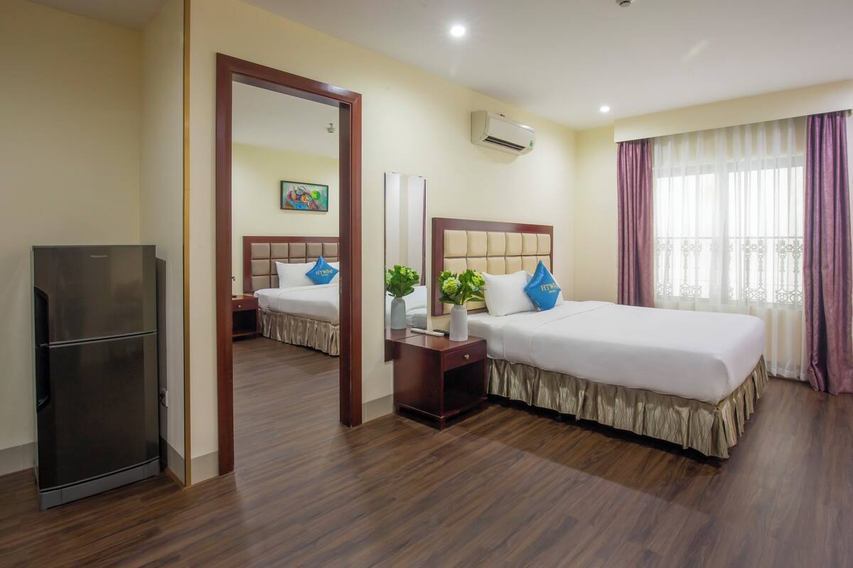 A hotel room with a bed, bedside table, mirror, air conditioning unit, and a refrigerator.