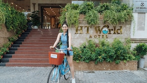 A person on a bicycle in front of the HT World Hotel entrance, with a staircase leading to the building. - Sea Front Hotel (Da Nang)