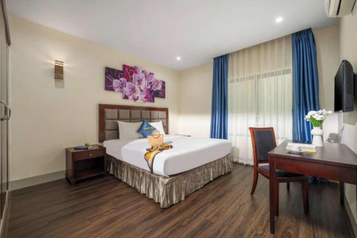 A hotel room with a bed, bedside table, chair, desk, and a large window with curtains.