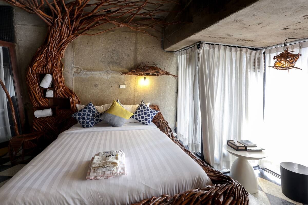 A bed with a tree branch design, a bedside table with books, and a hanging light fixture.