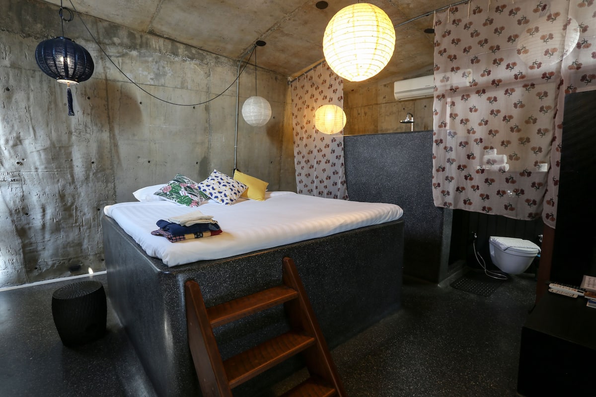 A compact room with a bed, a ladder, a toilet, and a sink.