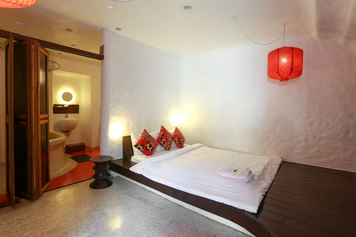 A hotel room with a bed, a wooden floor, a red lantern, and a bathroom visible through an open door.
