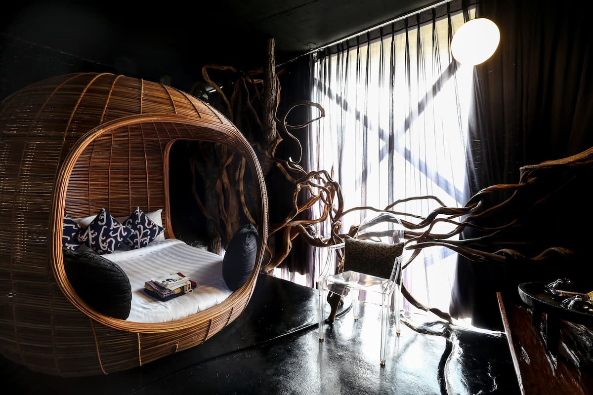 A room with a circular wicker bed, a clear chair, and a unique tree-like sculpture.
