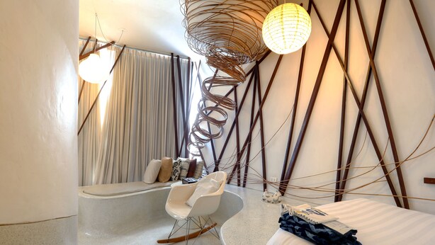 Una habitación de hotel moderna con una cama curvada, un sillón mecedora, una bañera y un diseño de pared original.