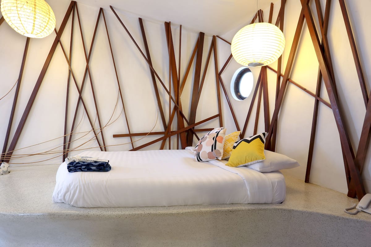 A modern bedroom with a bed, pillows, and a unique wooden wall design.