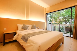 A bedroom with a large bed, a nightstand, and a view of a balcony with greenery. - The Kubu Hotel (Kuta)