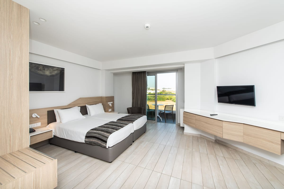 A modern hotel room with a large bed, a TV, and a balcony with a view.