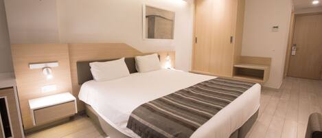 A modern hotel room with a large bed, bedside tables, a wardrobe, and a mirror.