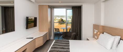 A modern hotel room with a large bed, a desk, a television, and a balcony with a table and chairs.