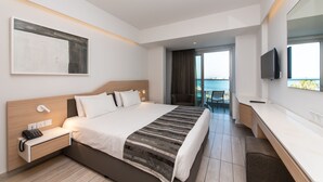 Moderni hotellihuone, jossa on suuri sänky, yöpöytä puhelimella, taulutelevisio ja suuri ikkuna, josta avautuu näkymä merelle.