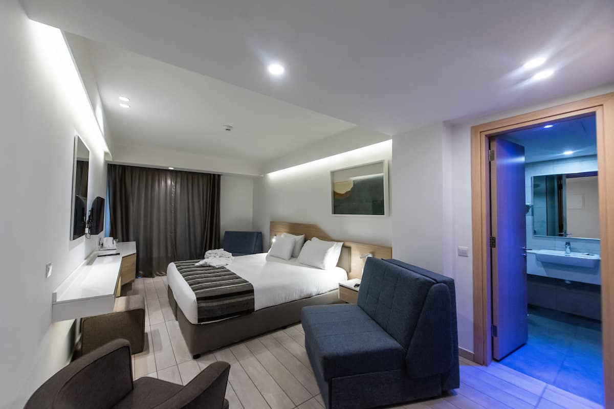 A modern hotel room with a bed, a desk, a chair, and a sofa.