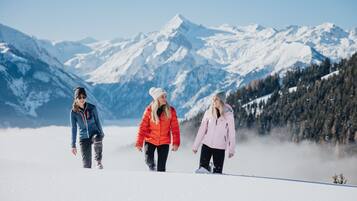 Tres personas caminando por un sendero cubierto de nieve, con montañas al fondo.
