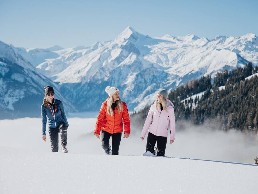 Tres personas caminando por un sendero cubierto de nieve, con montañas al fondo.