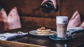 Un desayuno con tortitas, almíbar y una taza de café sobre una mesa.