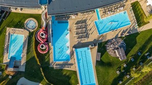 An aerial view of a hotel with multiple swimming pools, sun loungers, and a large circular water feature. - Lederer Boutique Hotel  (Kaprun)