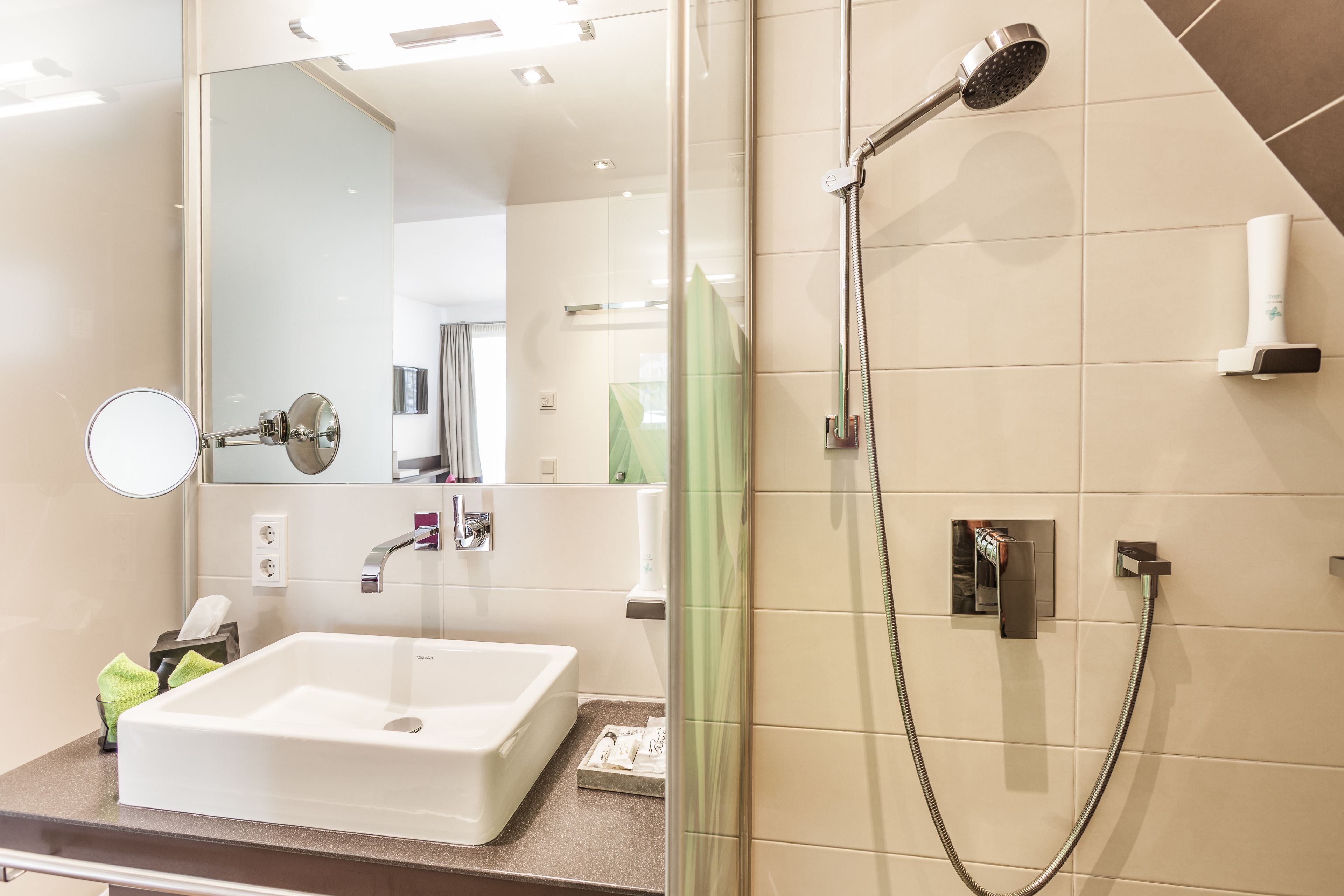 A modern bathroom with a large mirror, a white sink, and a shower with a handheld showerhead.