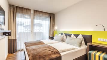 Une chambre d’hôtel moderne avec un grand lit, une table de chevet, un banc et une vue sur la ville à travers des rideaux transparents.