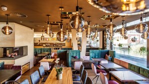 A modern restaurant with multiple seating areas, including booths and tables, and a variety of pendant lights. - Lederer Boutique Hotel  (Kaprun)