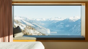 A room with a large window offering a view of snow-covered mountains and a lake. - Chetzeron (Crans)