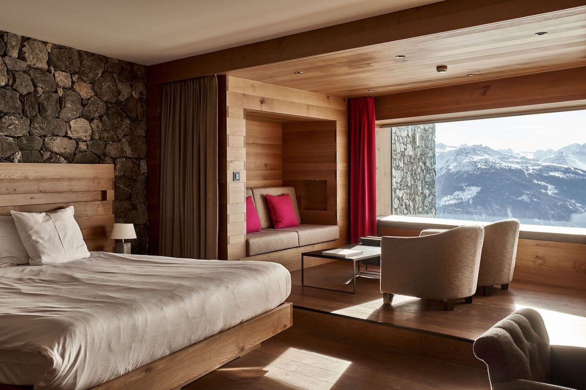 A modern hotel room with a large bed, a sofa, and a view of mountains.