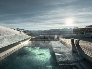 A hot spring area with a wooden deck, a bench, and a view of snow-covered mountains.