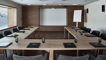 Un salón de conferencias con una larga mesa, sillas, computadoras portátiles y una pantalla de proyector.