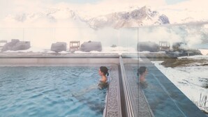 A hot spring bath with a glass enclosure, a wooden chair, and a view of snow-capped mountains. - Chetzeron (Crans)
