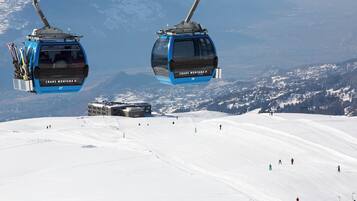 Eine Seilbahn mit Gondeln, beschriftet mit 'CRANS MONTANA', und ein schneebedeckter Hang mit Skifahrern.
