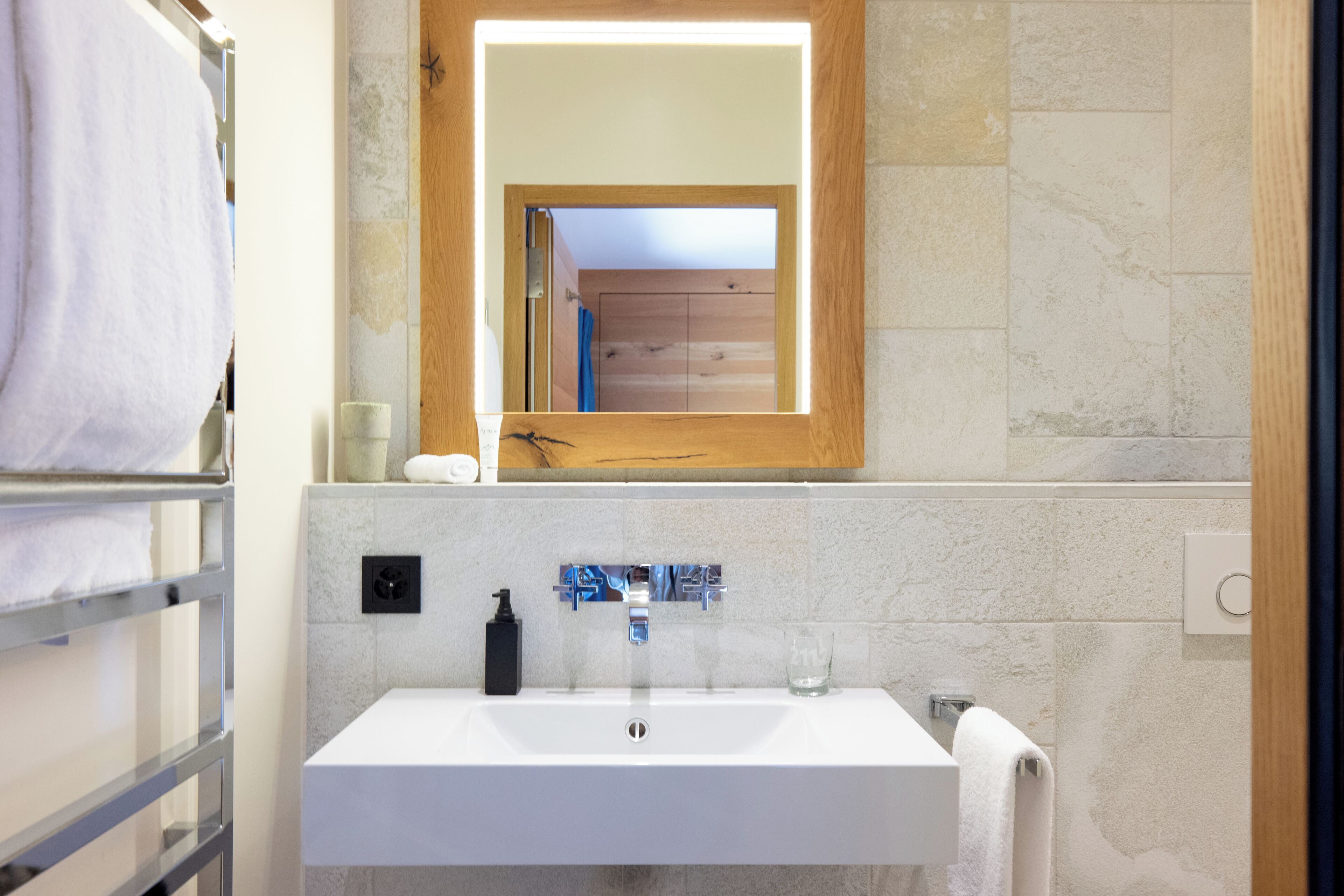A bathroom with a white sink, a mirror with a wooden frame, a towel rack, and a glass of water.