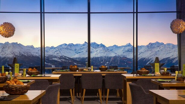 A dining area with a mountain view, tables with chairs, and various food items. - Chetzeron (Crans)