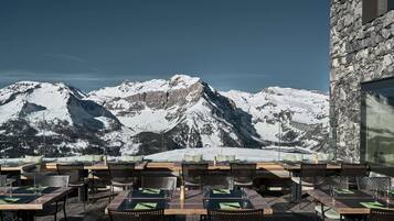 A terrace with tables and chairs, overlooking snow-covered mountains.