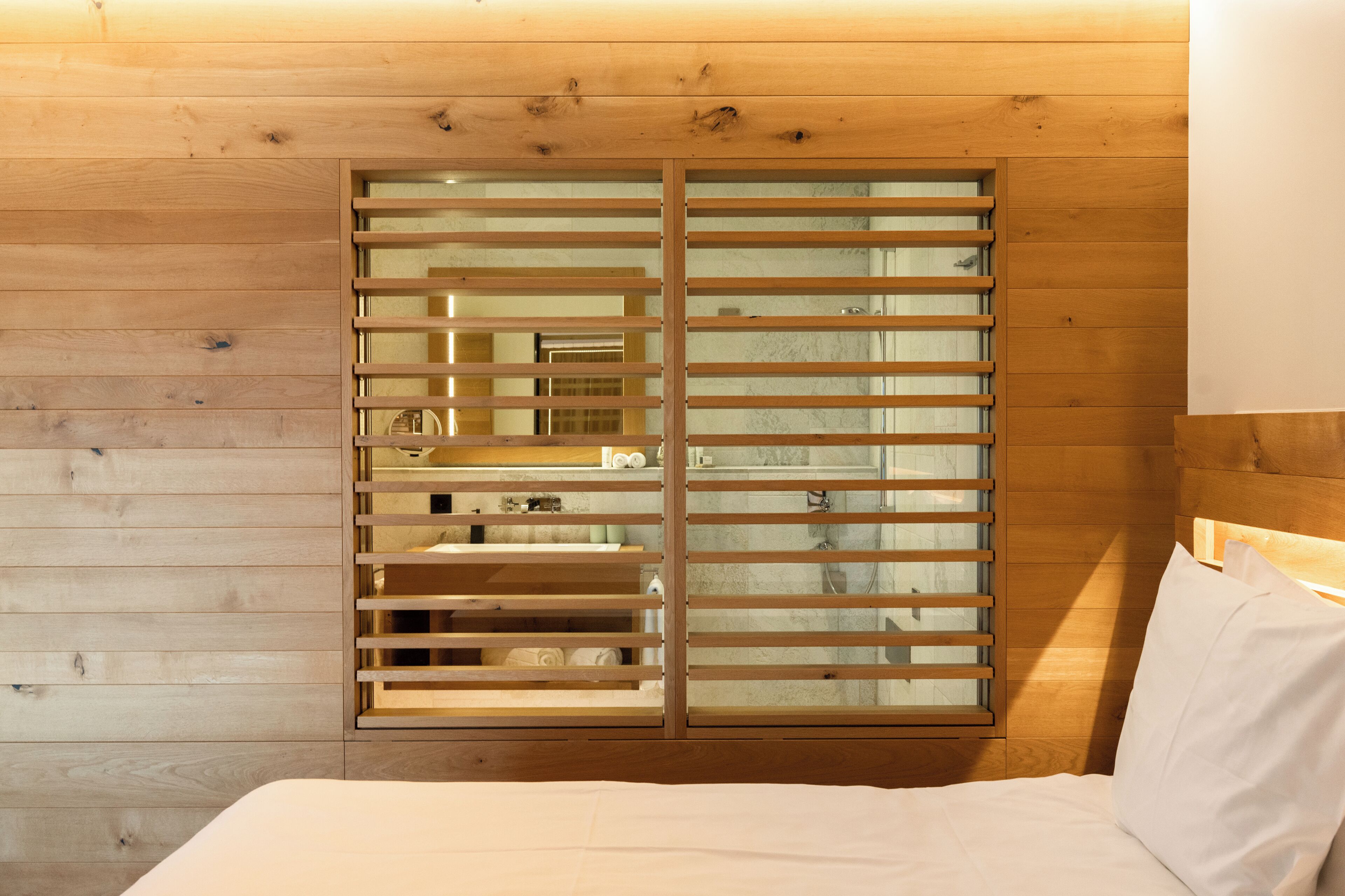 A bedroom with wooden panel walls, a bed with white bedding, and a window with horizontal blinds.
