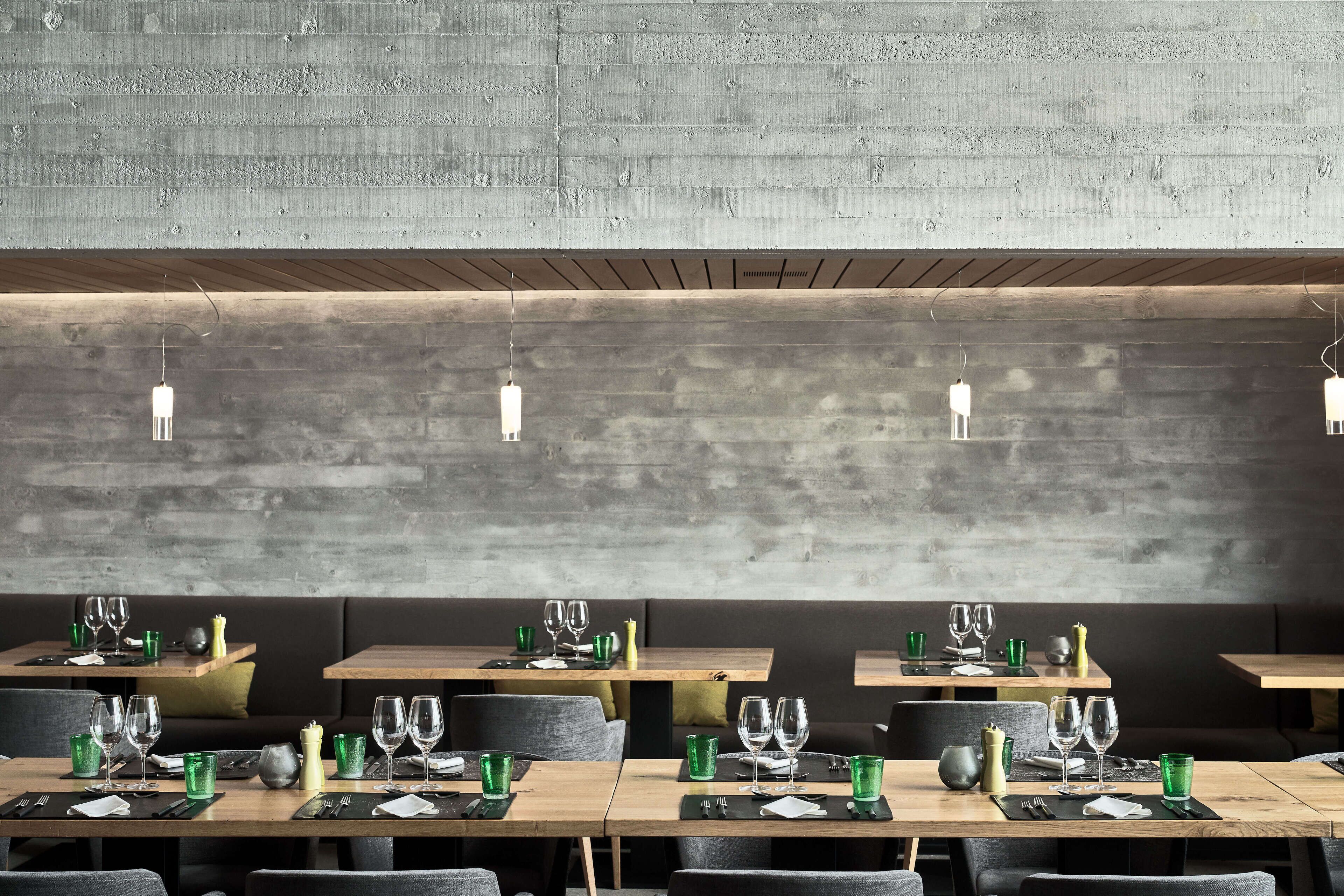 Ein Restaurant mit Holztischen und -stühlen vor einer rustikalen Betonwand.