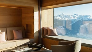 A cozy cabin interior with a sofa and armchairs, a wooden wall, and a window offering a mountain view. - Chetzeron (Crans)