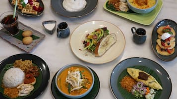 Forskellige retter på et bord, herunder en tallerken med nudler, ris og kød, en skål suppe samt flere andre tallerkener med forskellig mad.