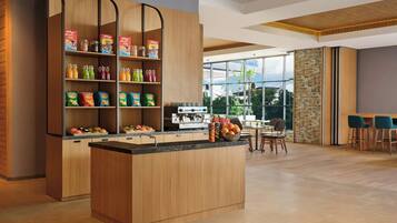 A modern kitchen with wooden cabinetry, a central island, and a breakfast bar. There are shelves with various food items and a large window providing a view of the outdoors.