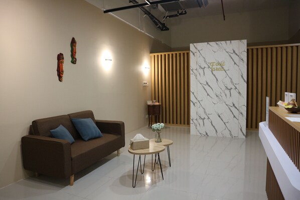 A modern reception area with a brown sofa, a small round table with a tissue box, and a wooden panel wall with a marble-like design. - Four Points by Sheraton Batam (Batam)