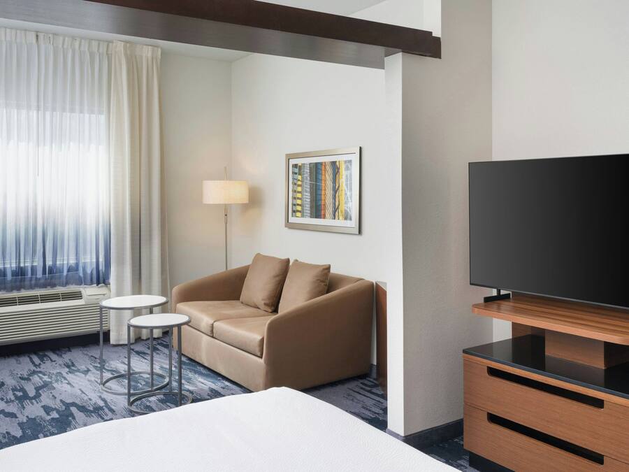 Habitación de hotel con cama, sofá, dos mesitas, televisor y un cuadro en la pared.