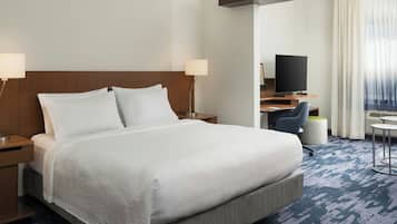 Habitación de hotel con una cama grande, dos mesitas de noche, un escritorio con silla, un televisor y vistas al exterior por una ventana.