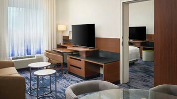 Habitación de hotel con escritorio, dos sillas, televisión, cama y mesa de vidrio.