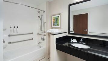 Une salle de bain moderne avec une baignoire, un grand miroir et un lavabo sur un plan de toilette noir.