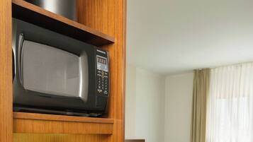 A hotel room with a microwave on a shelf, a coffee maker, and a trash bin. There are two beds with white linens and a blue patterned carpet.
