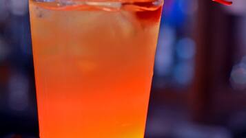 A tall glass with a gradient color from yellow to orange, a cherry on a straw, and a blurred background.