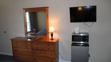 A wooden dresser with a mirror, a lamp, a television mounted on the wall, and a microwave on a stand.