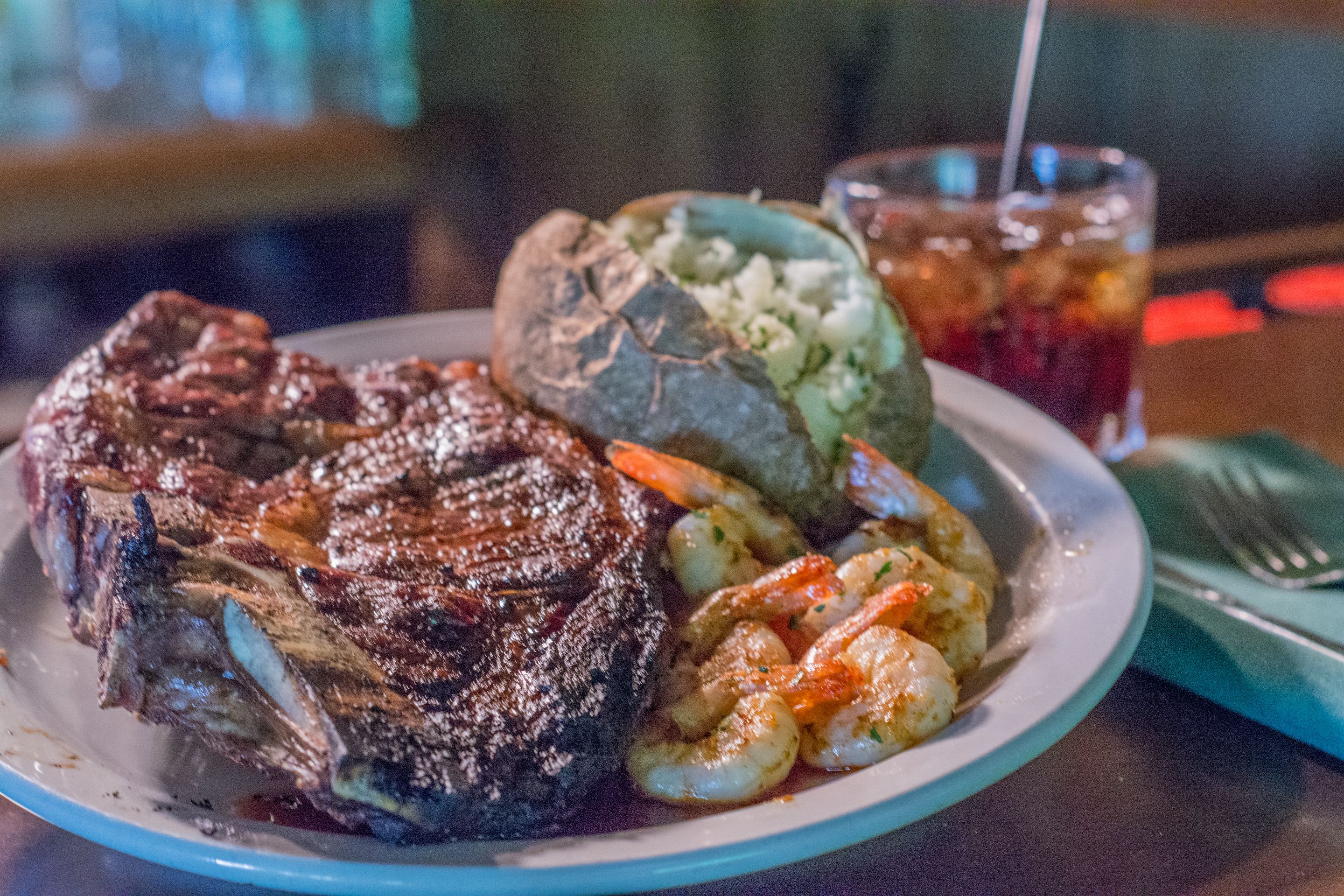 A plate with a steak, shrimp, and a baked potato.