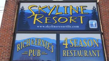 Placa para o Skyline Resort com um endereço de site e um ícone do Facebook. Abaixo, placas indicam o Rich & Ernie's Pub e um Restaurante para todas as estações.