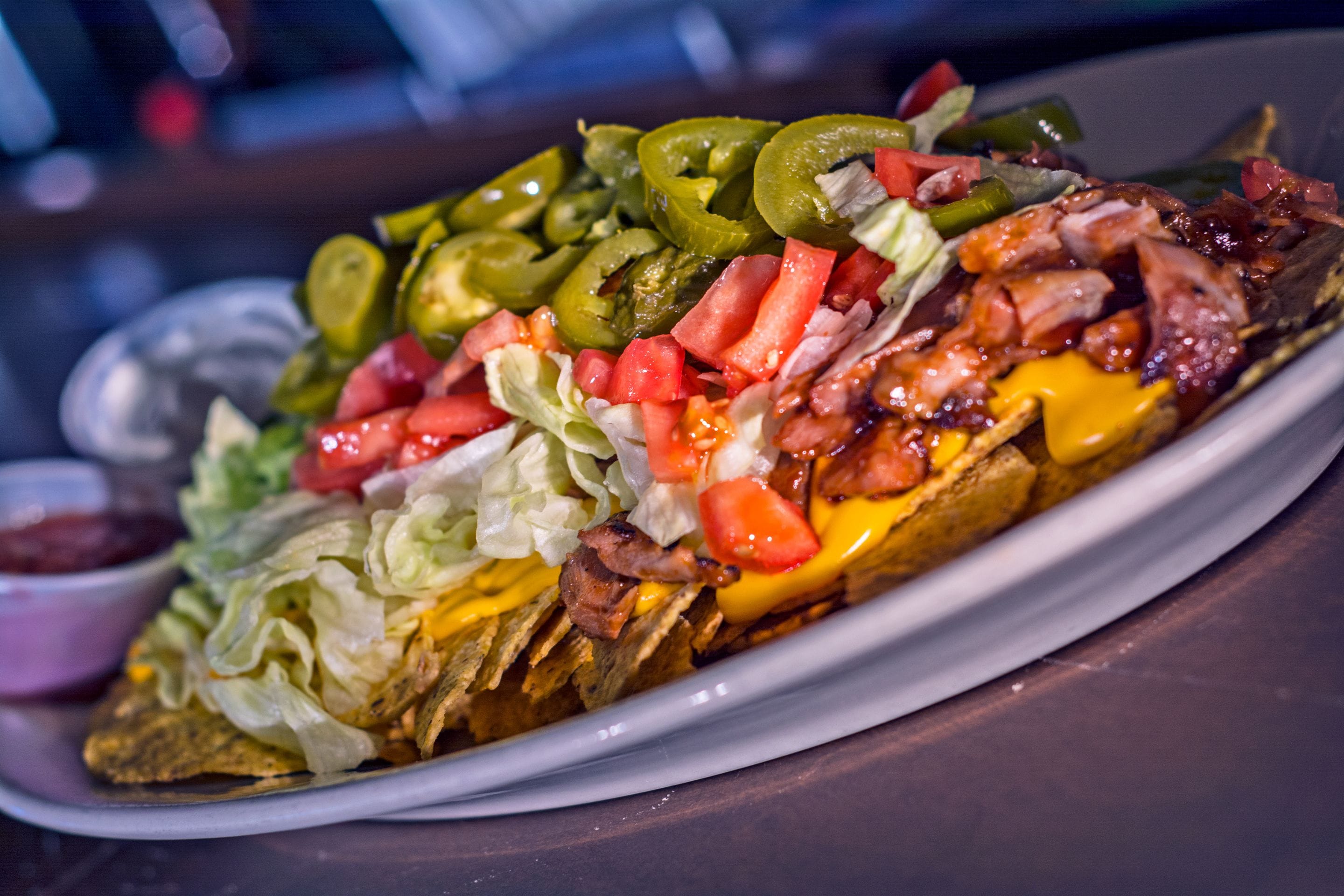 A plate of nachos topped with cheese, lettuce, tomatoes, jalapeños, and meat.