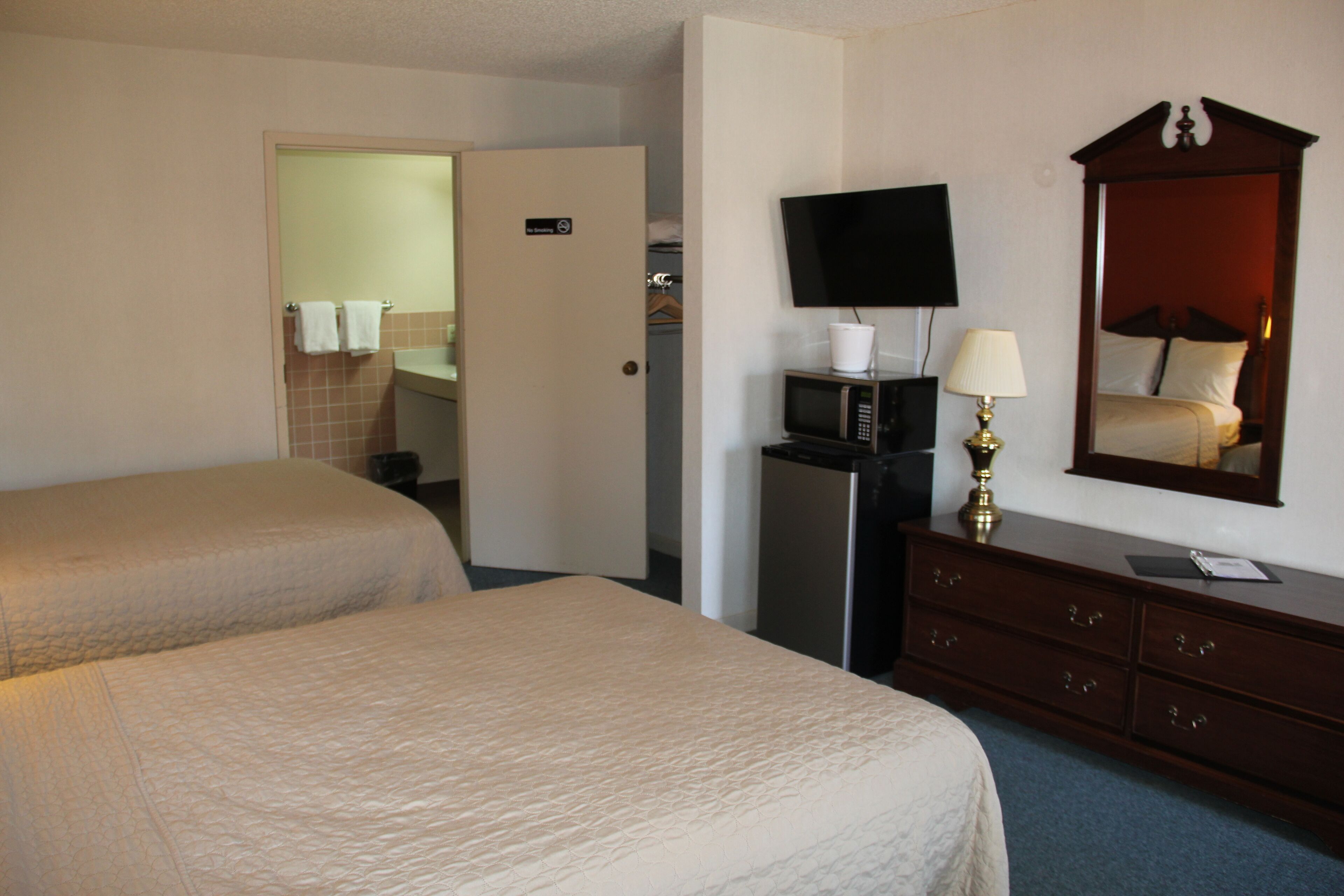 Hotelkamer met twee bedden, een televisie, een magnetron, een dressoir en een badkamer zichtbaar door een open deur.