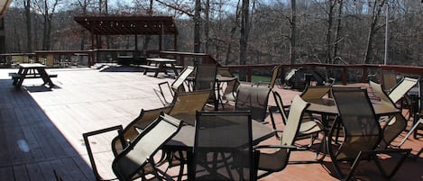 A deck with picnic tables and chairs, surrounded by trees.