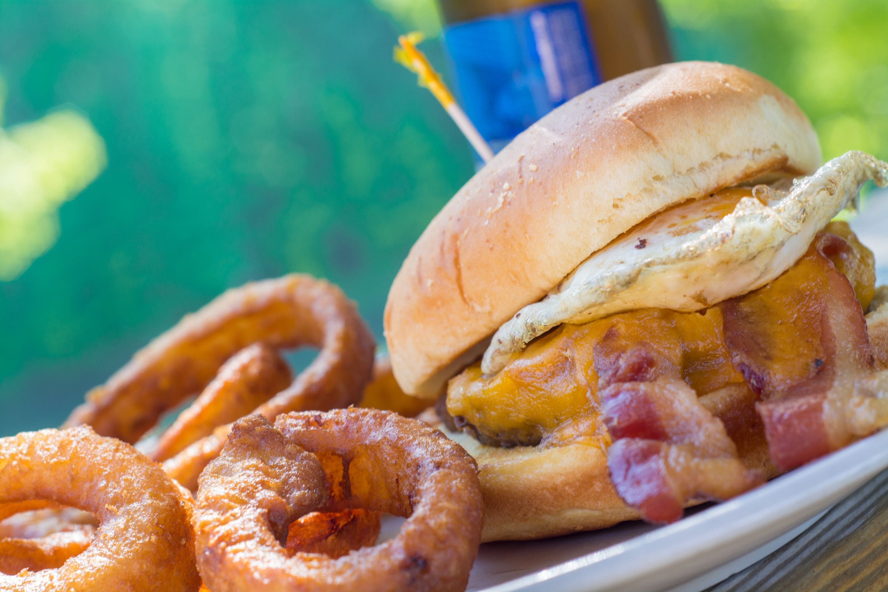 A plate with a sandwich, bacon, egg, and onion rings.